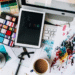 Messy desk with digital device, coffee, art tools