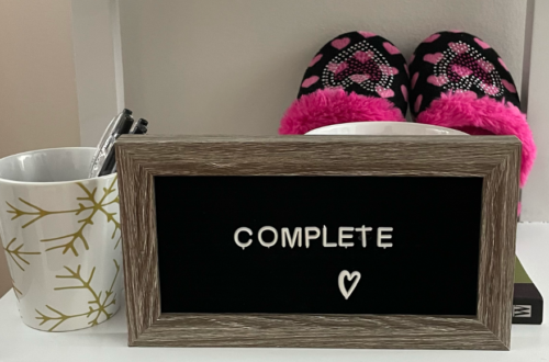 COMPLETE sign board in my office with pink kid slippers and a coffee mug holding pens.