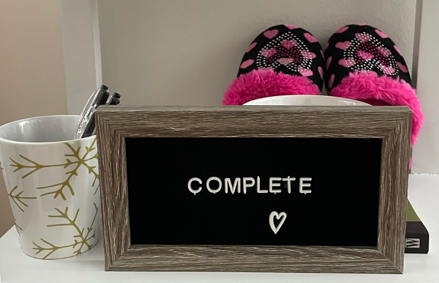 COMPLETE sign board in my office with pink kid slippers and a coffee mug holding pens.