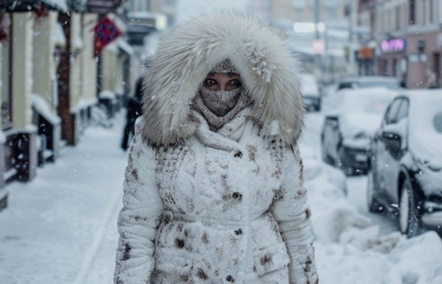 Beautiful black woman, in the falling snow, in white winter coat with fur hood, and face covering.