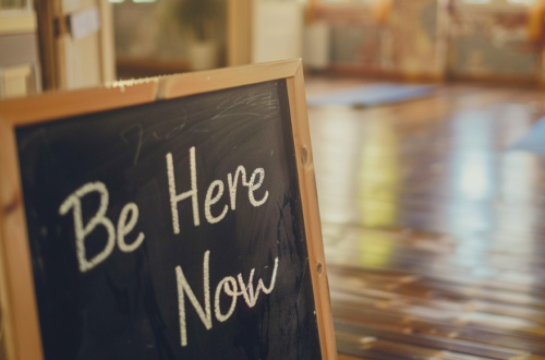 'Be Here Now' sign on board as in a yoga room.