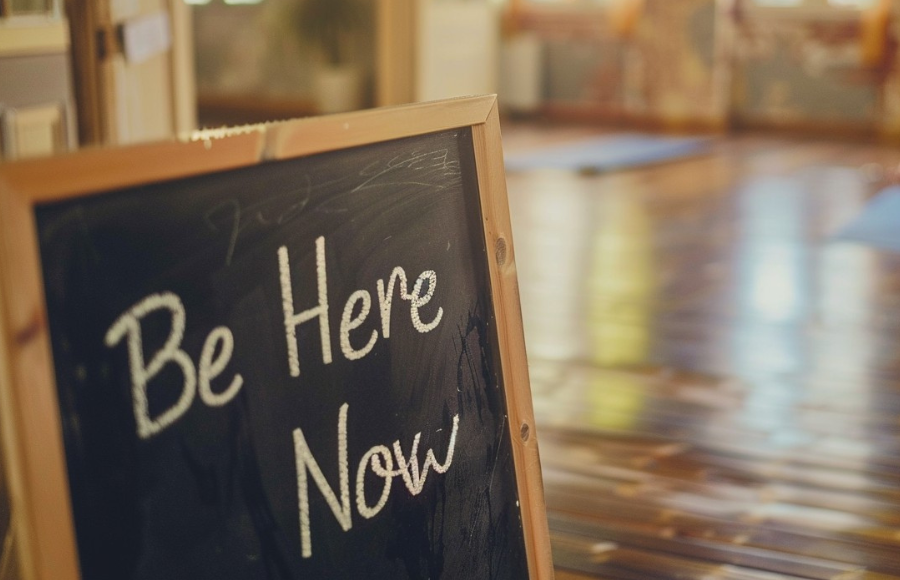 'Be Here Now' sign on board as in a yoga room.