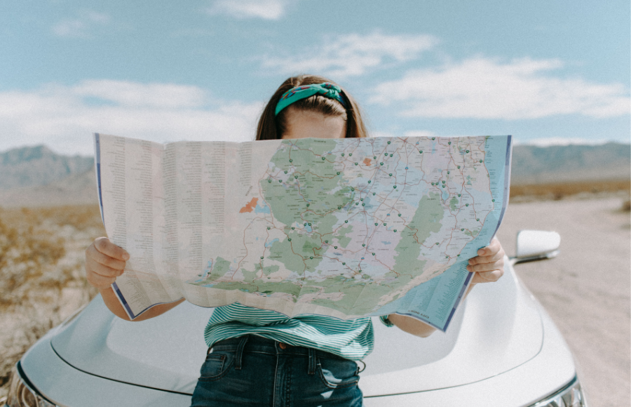 Woman sitting on car in desert with her face burried in a map