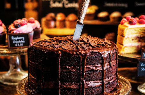 A dark mysterious layered fudge cake with a knife in it, dead center, no candles in a cake shop with other cakes around.