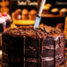 A dark mysterious layered fudge cake with a knife in it, dead center, no candles in a cake shop with other cakes around.
