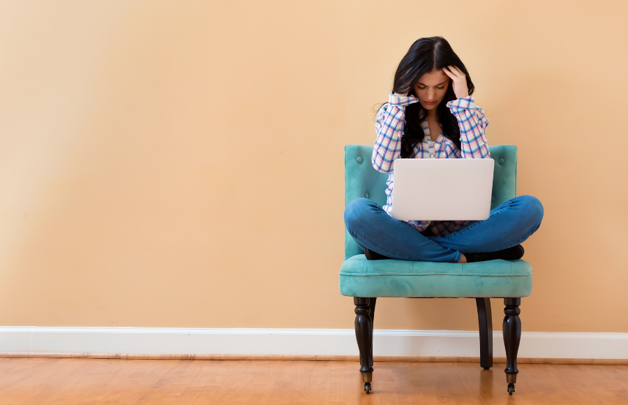 SincerelyIreneb, Vote, November midterms 2026, woman sitting on a blue plush chair, crossed legs with laptop in her lap, her hands in her long brown hair, visibly confused.